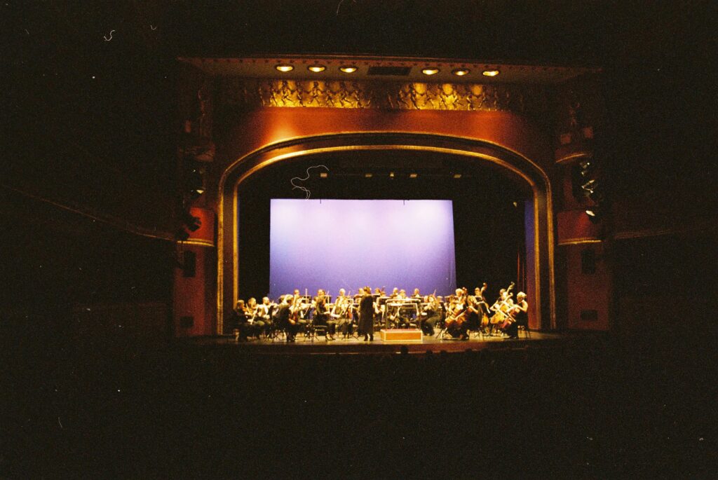 A live orchestra performs under spotlights on a grand theater stage, showcasing musical artistry.